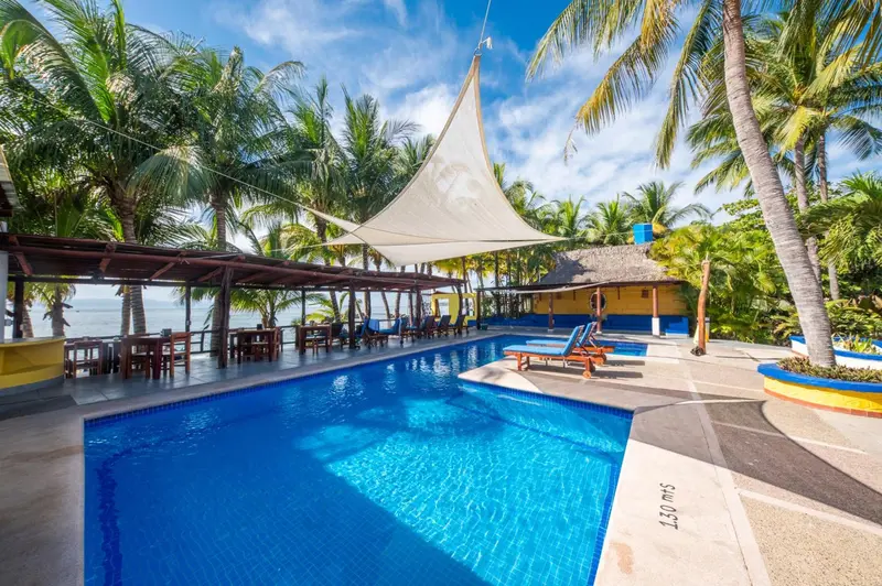 Piscine bleue bordée de chaises longues sous un abri ombragé.