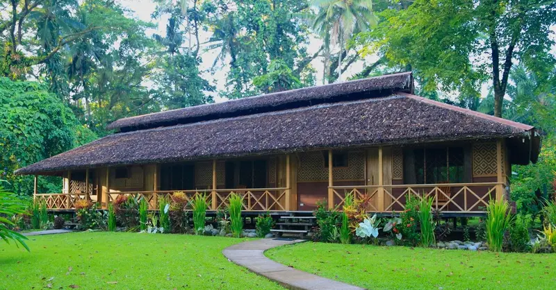 Bâtiment en bois sur pilotis avec toiture de chaume et végétation luxuriante.