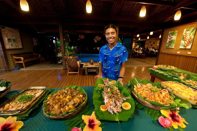 Une personne souriante présente un buffet de plats variés dans un espace de restauration extérieur.