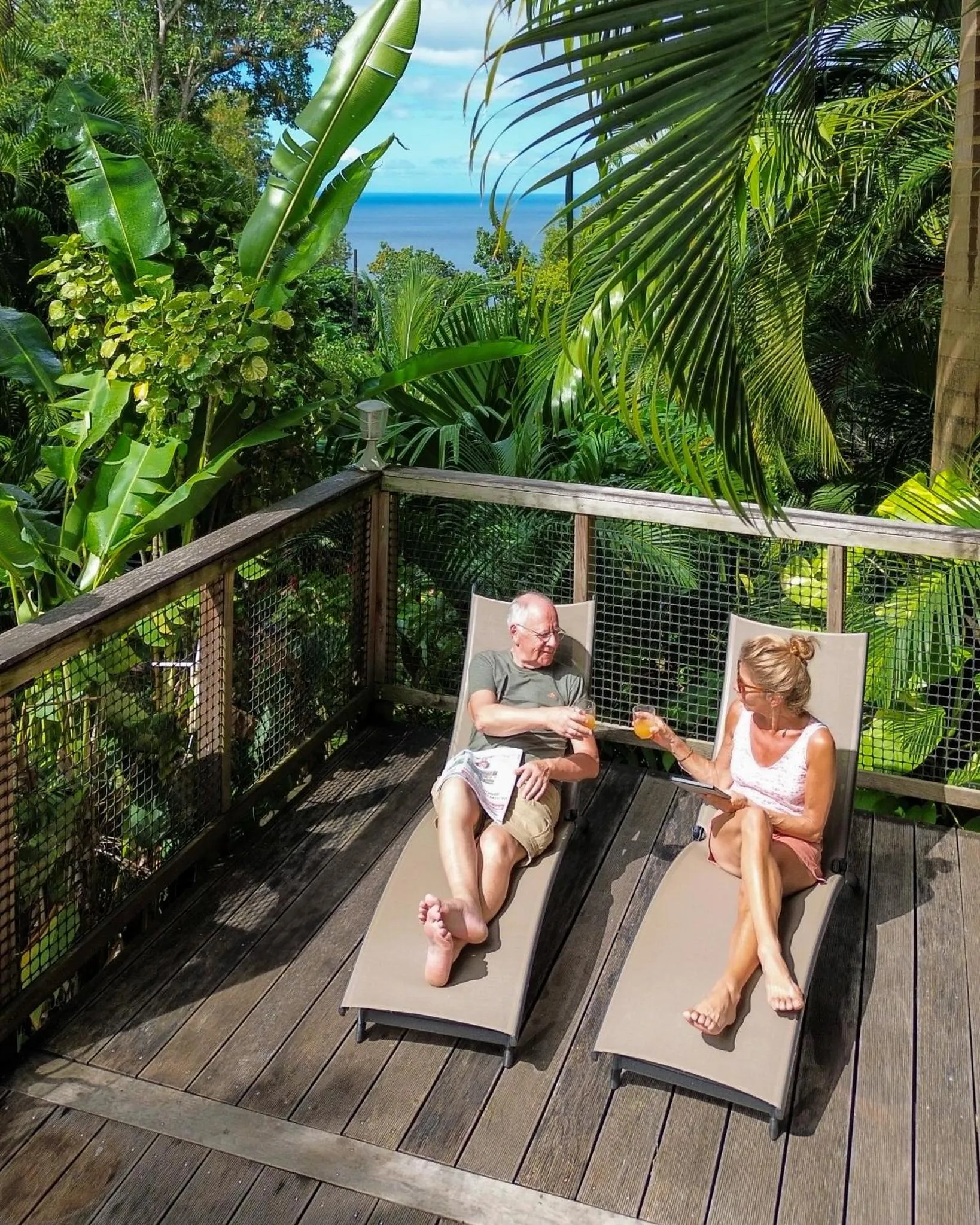 Un couple se détend sur des transats en bois sur une terrasse ensoleillée.
