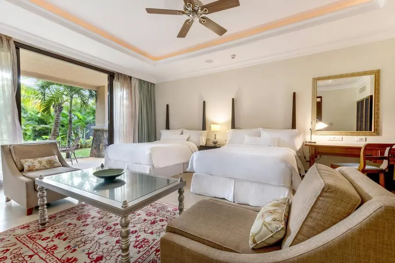 Chambre lumineuse avec deux lits et un coin salon donnant sur une végétation luxuriante.