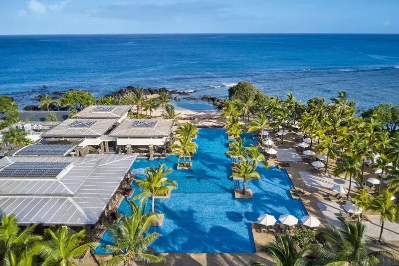 Vue aérienne d'une piscine d'hôtel bordée de palmiers et donnant sur la mer.