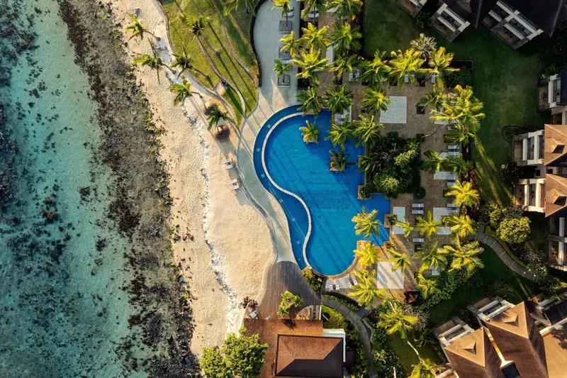 Vue aérienne d'une piscine turquoise bordée d'une plage de sable et de végétation tropicale.