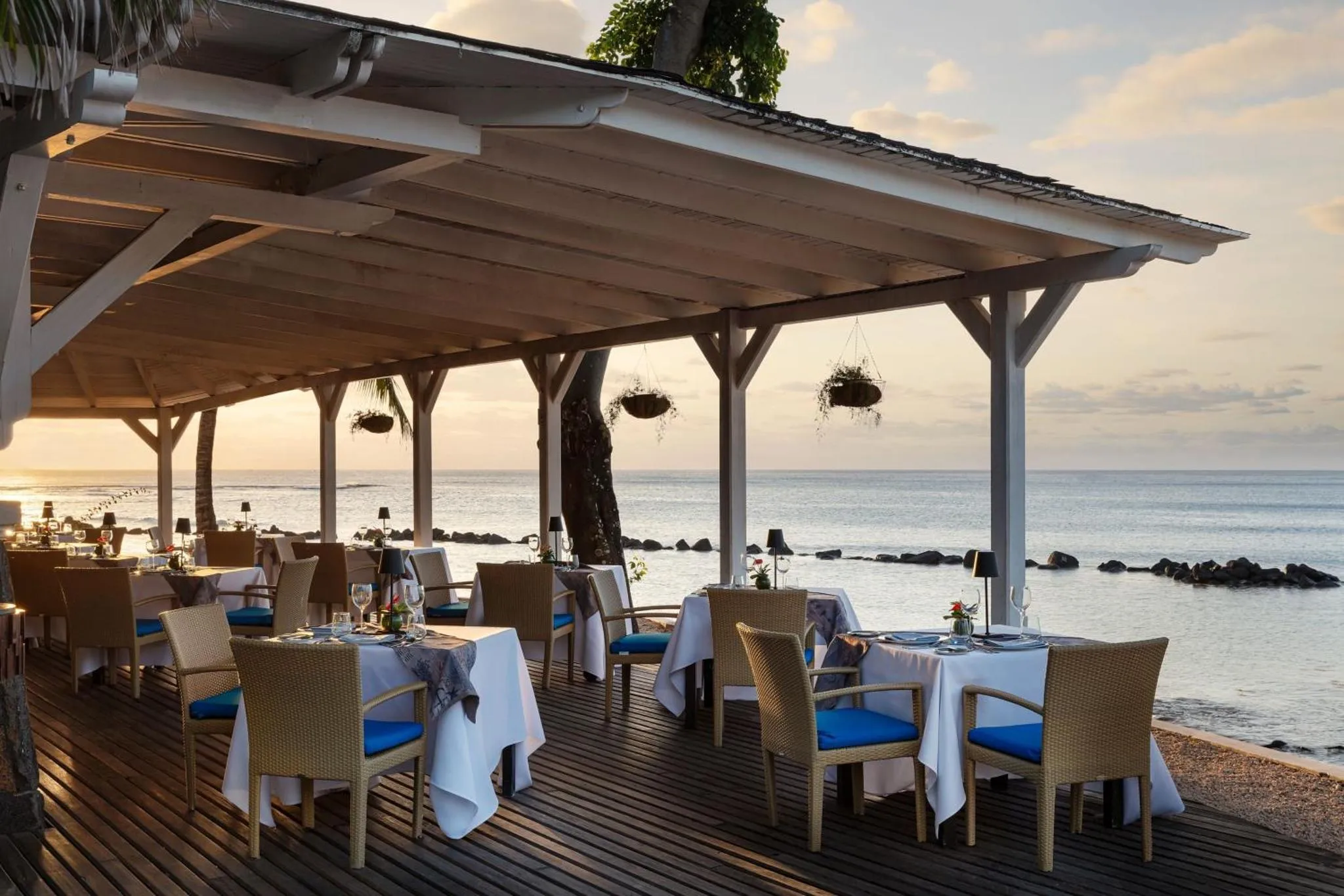 Tables de restaurant en terrasse face à la mer au coucher du soleil.