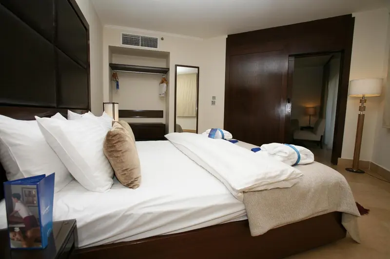 Une chambre lumineuse avec un grand lit recouvert d'une courtepointe blanche et de coussins.