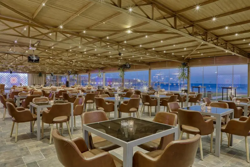 Une salle de restaurant spacieuse avec des tables et des chaises en cuir, donnant sur une vue nocturne de la mer.