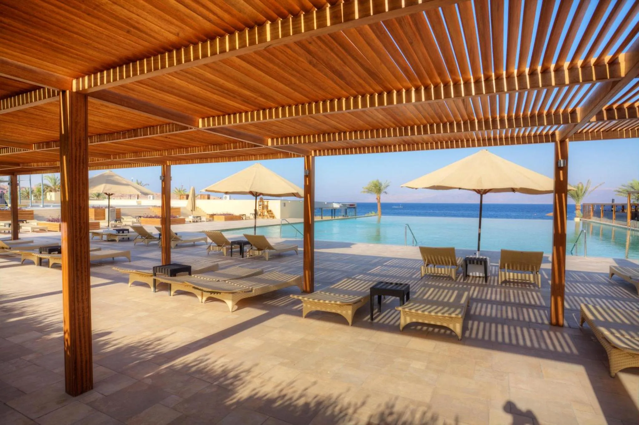 Terrasse ombragée avec transats et piscine à débordement.