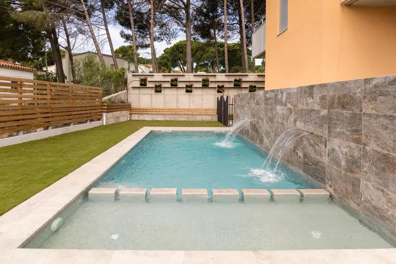 Une piscine rectangulaire avec une cascade artificielle dans un jardin soigné.