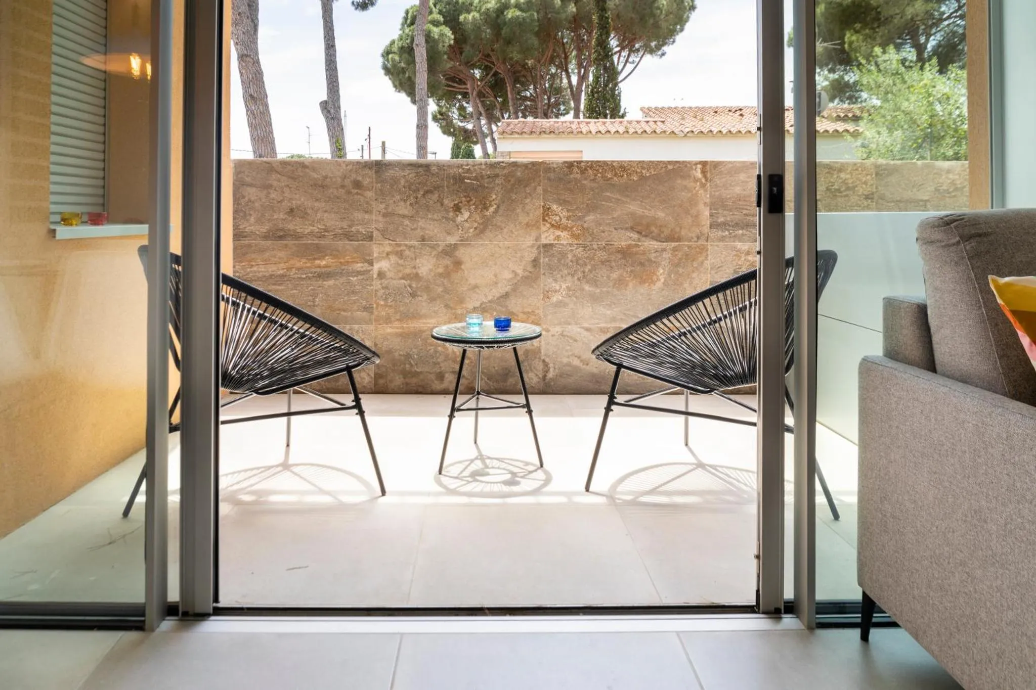 Deux fauteuils noirs et une petite table en verre sur une terrasse carrelée.
