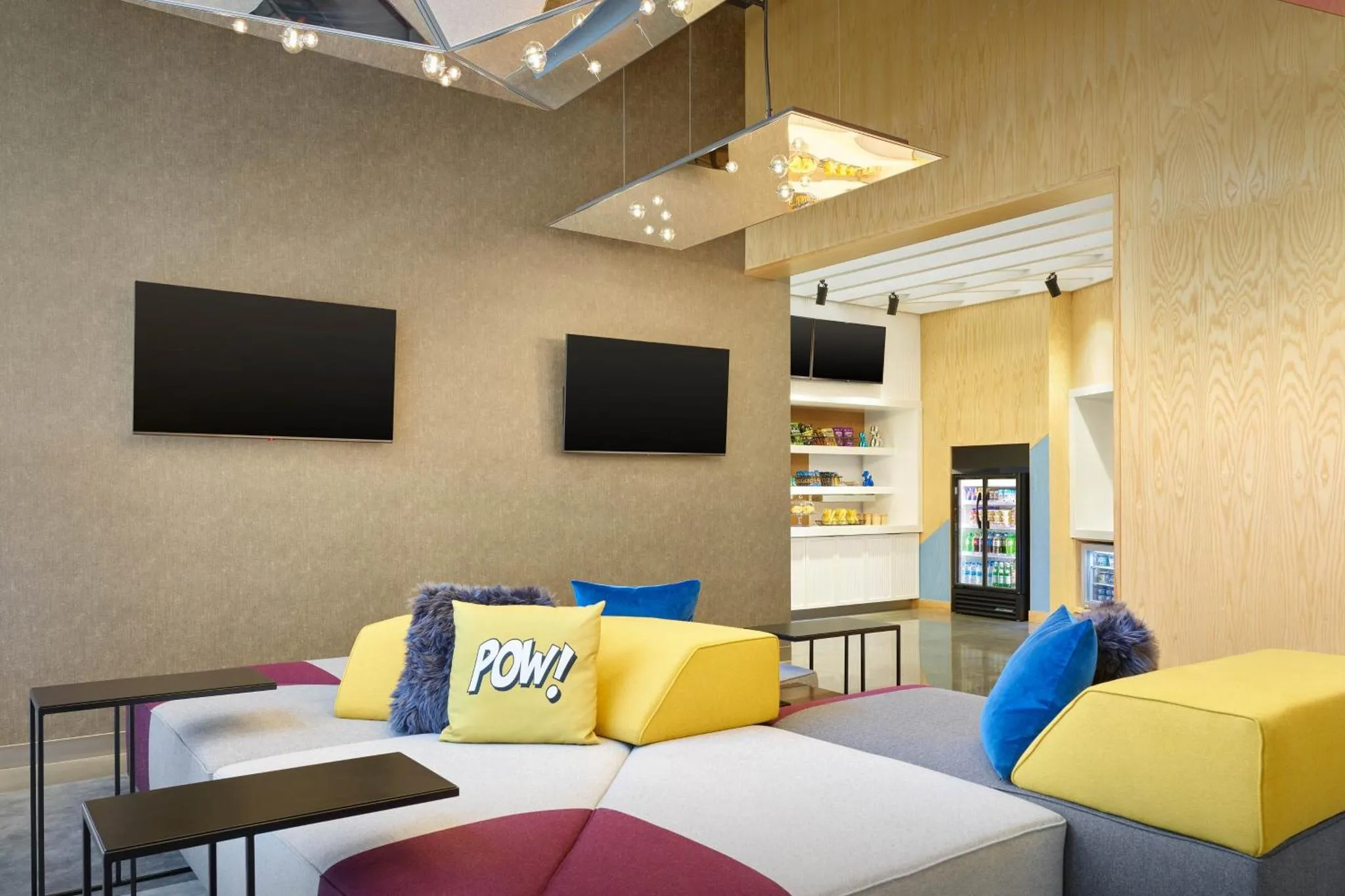 Espace de détente coloré avec canapés et téléviseurs muraux.