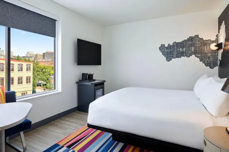 Une chambre lumineuse avec un grand lit et une fenêtre donnant sur la ville.