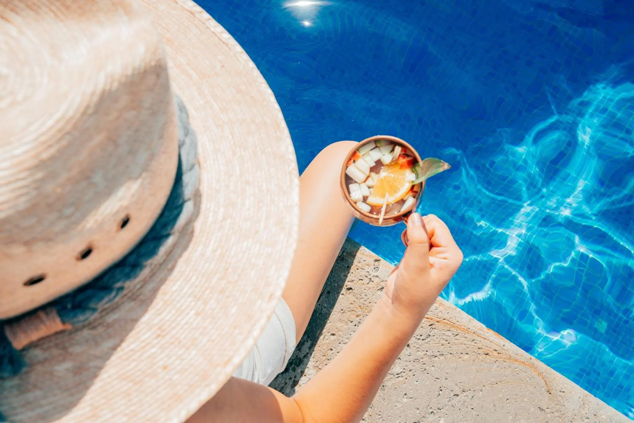 Une personne déguste une boisson au bord d'une piscine ensoleillée.