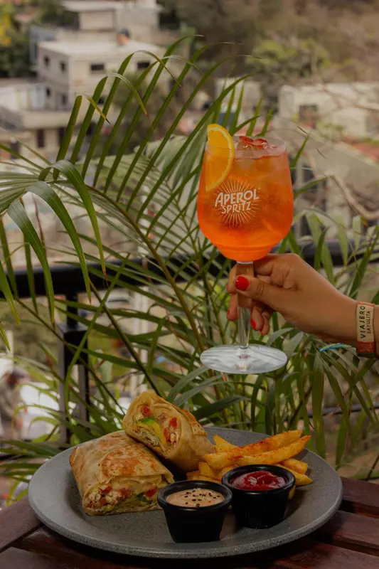Un cocktail orange et une assiette de nourriture sont servis sur une table en extérieur.
