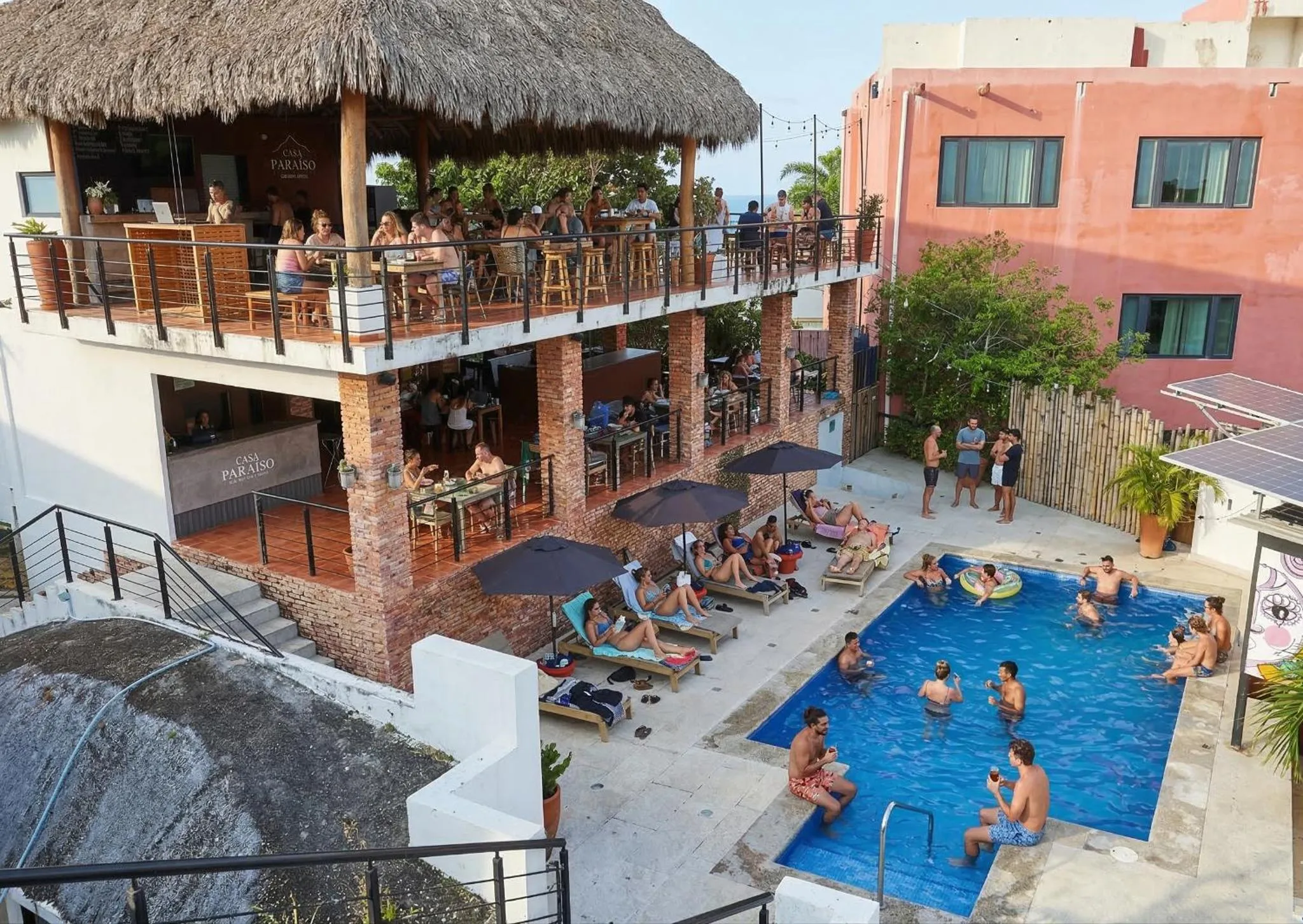 Terrasse ombragée avec tables et chaises, surplombant une piscine et un espace de détente.