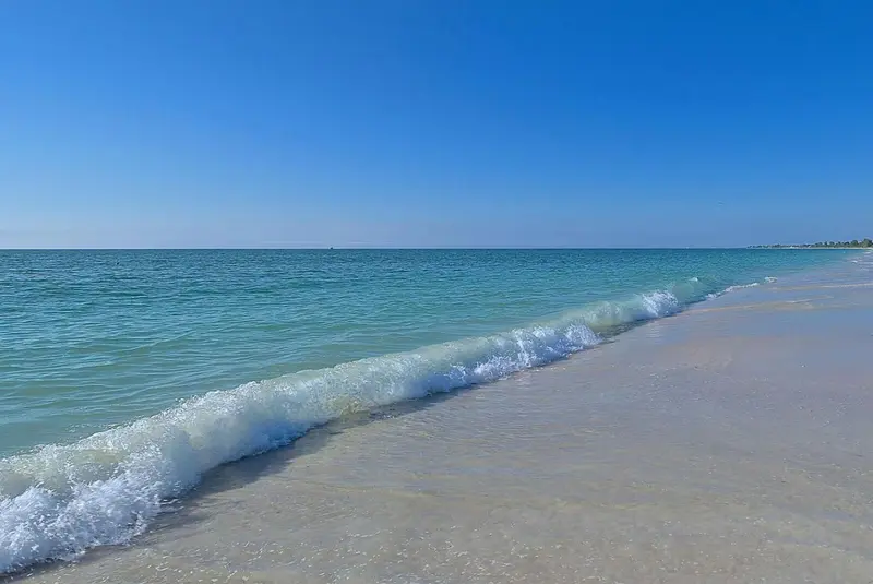 Vague déferlant sur une plage de sable blanc sous un ciel bleu.