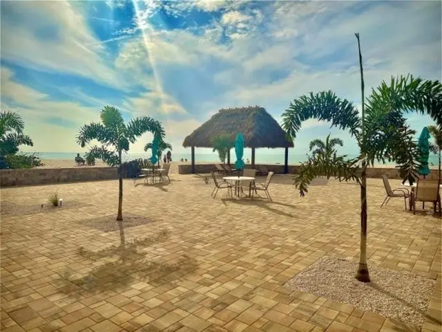 Terrasse pavée avec mobilier de jardin et abri de chaume en bord de mer.