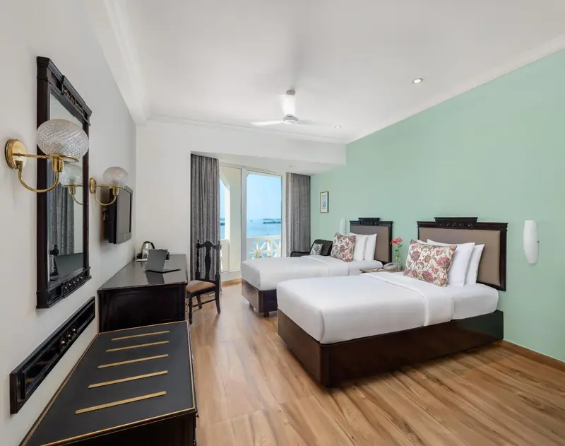 Chambre lumineuse avec deux lits simples et vue sur la mer.