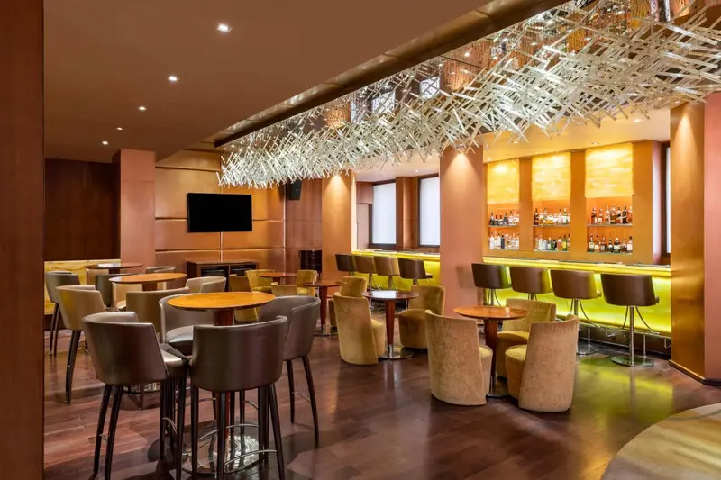 Un bar moderne avec des tabourets et des tables basses sous un luminaire décoratif.