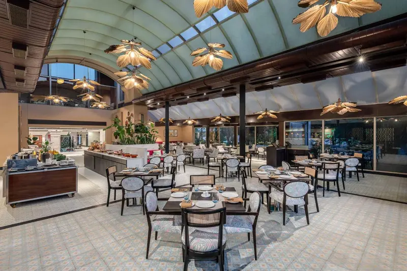 Une grande salle de restaurant lumineuse avec des tables dressées et un buffet.