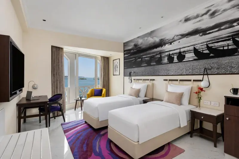 Chambre lumineuse avec deux lits simples et vue sur la mer.