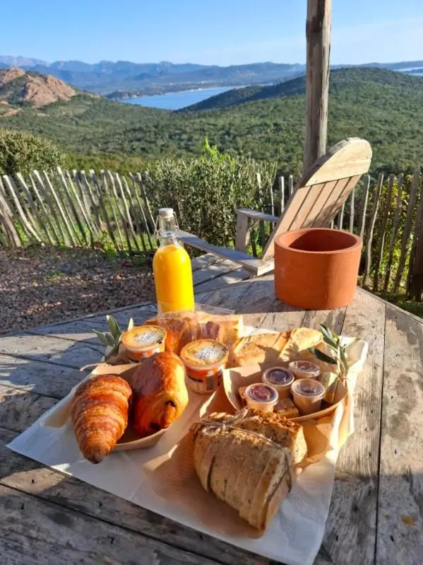 Une table en bois présente un petit-déjeuner avec des viennoiseries et des fruits, sur une terrasse avec vue sur un paysage montagneux.