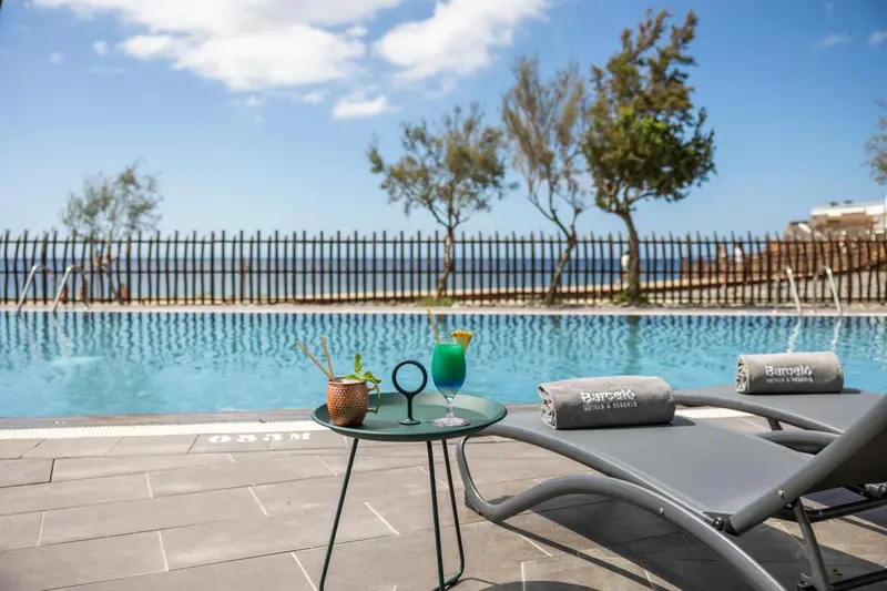 Transats et table basse avec boisson au bord d'une piscine.