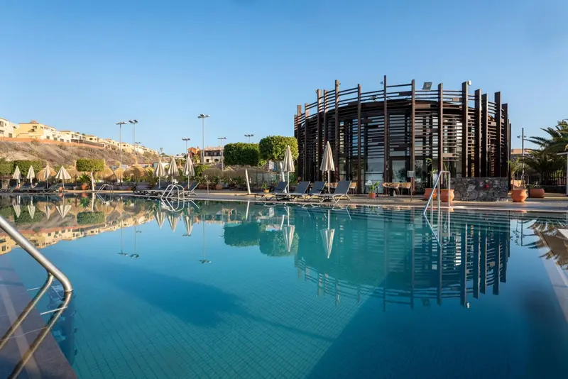Piscine turquoise reflétant un bâtiment moderne sous un ciel bleu clair.