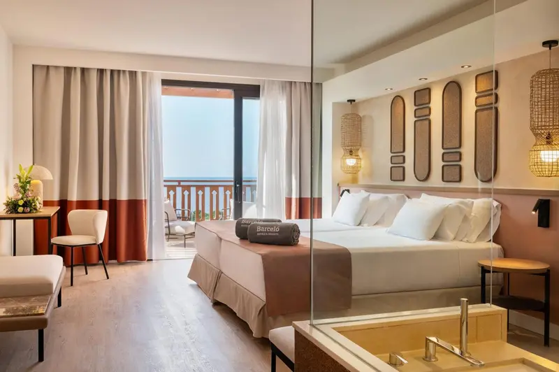 Chambre lumineuse avec un grand lit et un accès à une terrasse vue sur mer.