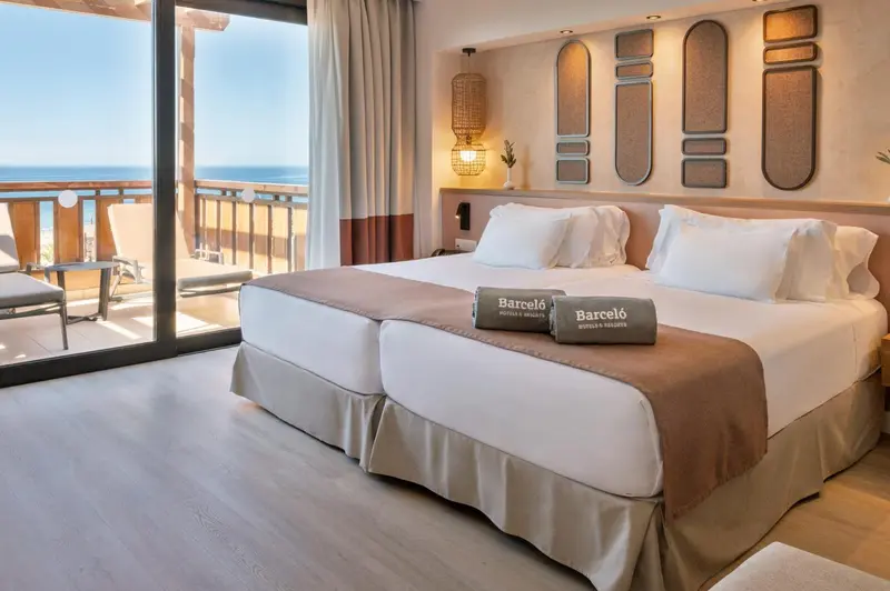 Chambre lumineuse avec un grand lit et un balcon donnant sur la mer.