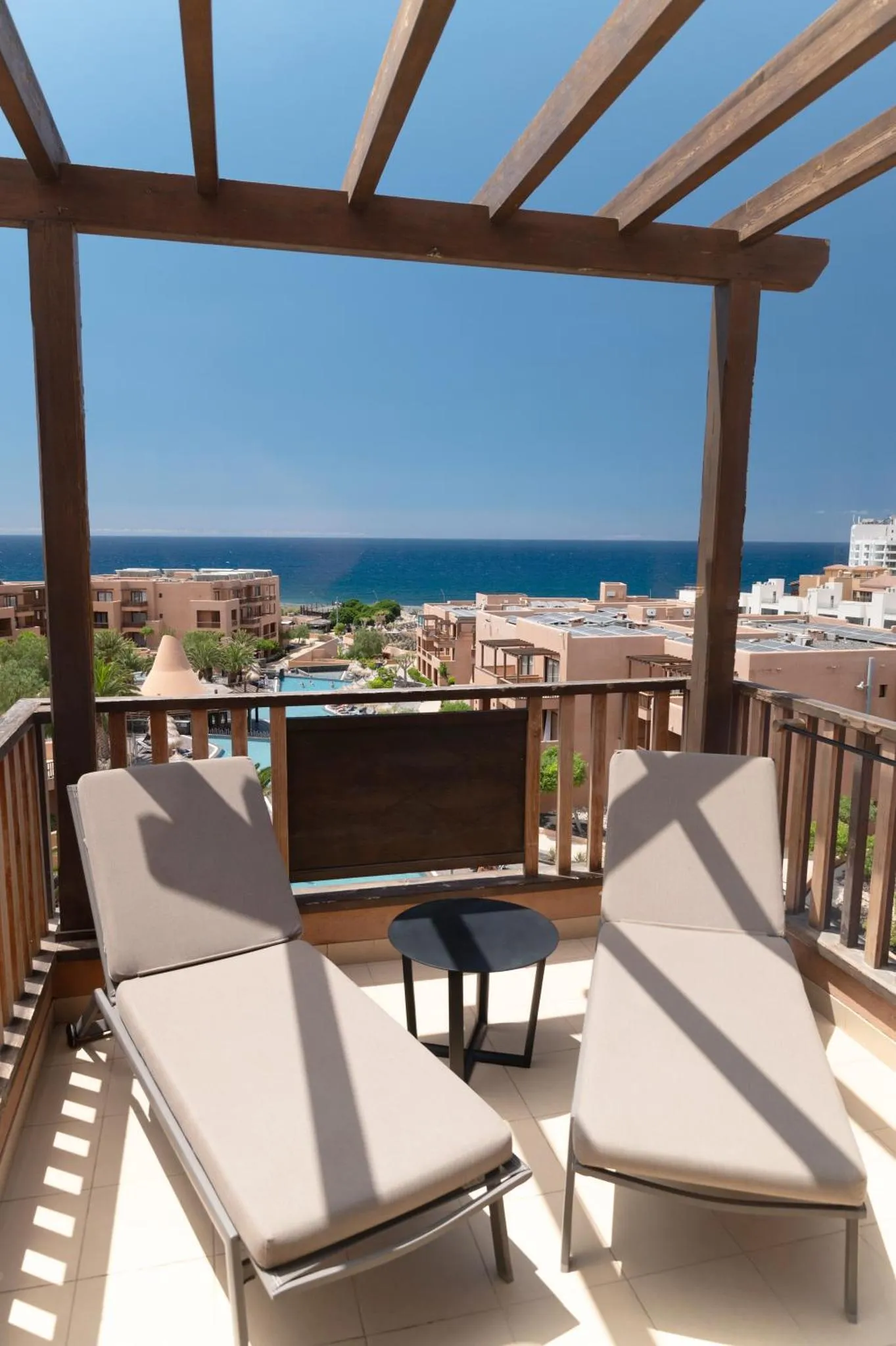 Deux transats et une table basse sur une terrasse avec vue sur la mer et un complexe hôtelier.
