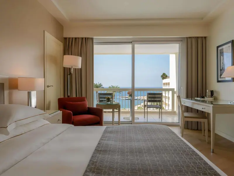 Une chambre lumineuse avec un lit et un accès à un balcon donnant sur la mer.