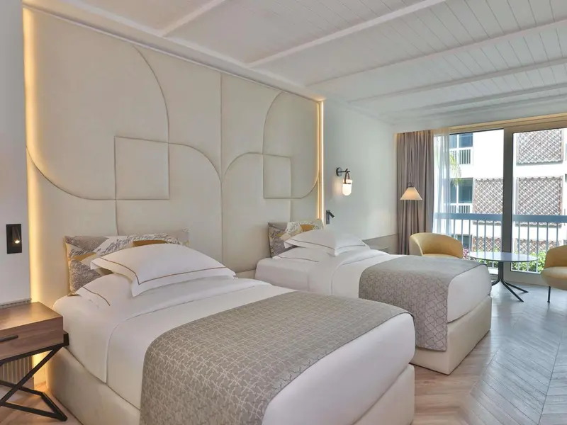 Une chambre lumineuse avec deux lits simples et un fauteuil.