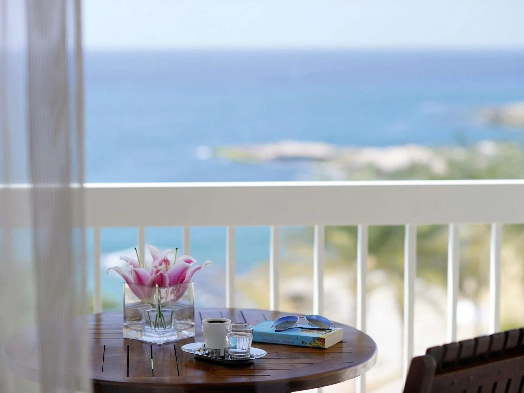 Une table ronde avec des fleurs et une tasse de café est posée sur une terrasse avec vue sur la mer.