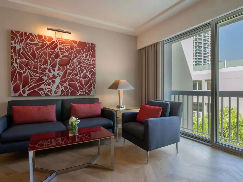 Un salon moderne avec canapés gris et coussins rouges, éclairé par une lampe sur une table basse.