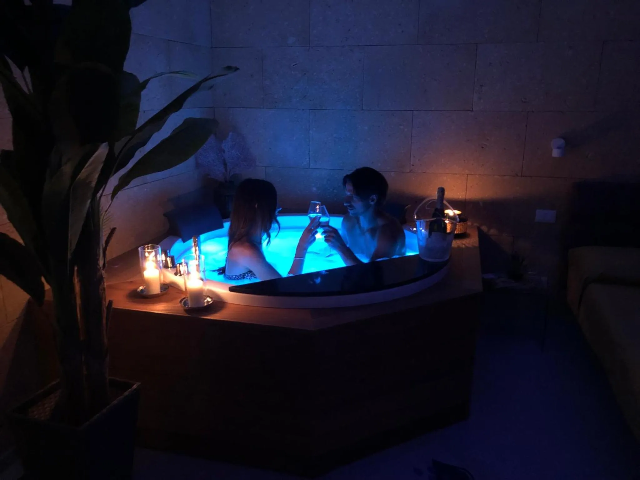 Un couple se détend dans un jacuzzi éclairé, avec des bougies et des boissons.