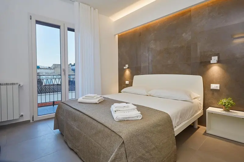 Chambre lumineuse avec un grand lit et un accès à un balcon.
