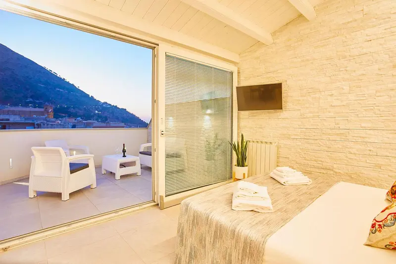 Une chambre lumineuse s'ouvre sur une terrasse avec vue sur la mer et les montagnes.