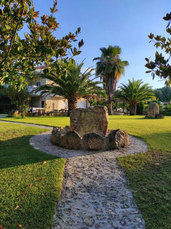 Un jardin verdoyant avec une fontaine en pierre et des palmiers.
