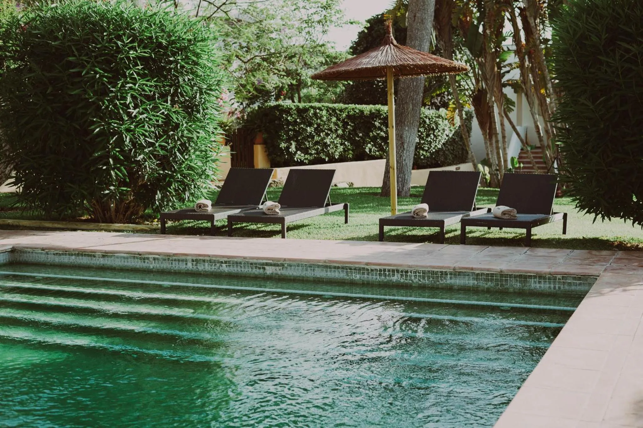 Transats et serviettes au bord d'une piscine turquoise dans un jardin luxuriant.