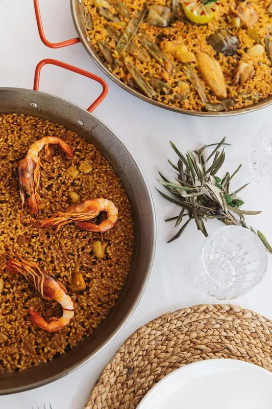 Vue rapprochée de paellas garnies de fruits de mer et d'herbes aromatiques sur une table.