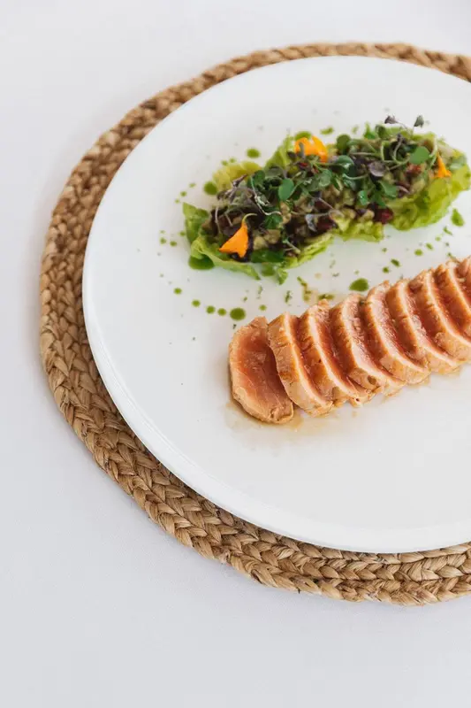 Assiette de poisson finement tranché accompagnée d'une salade et d'une sauce verte.