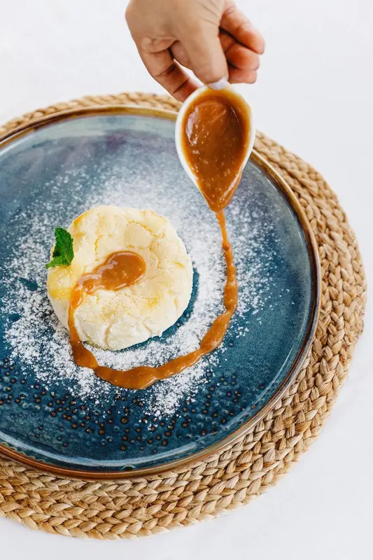 Une sauce caramel est versée sur une portion de glace à la vanille saupoudrée de sucre glace.