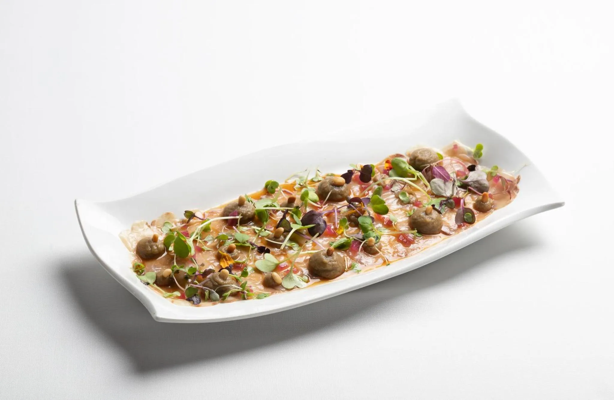 Présentation raffinée d'un plat de poisson cru agrémenté de légumes et de sauces.