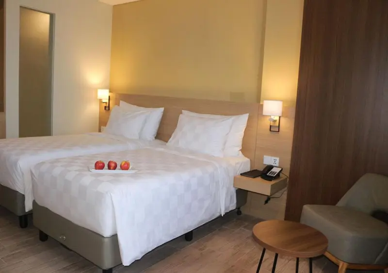Une chambre lumineuse avec un grand lit recouvert de draps blancs et des fruits frais.