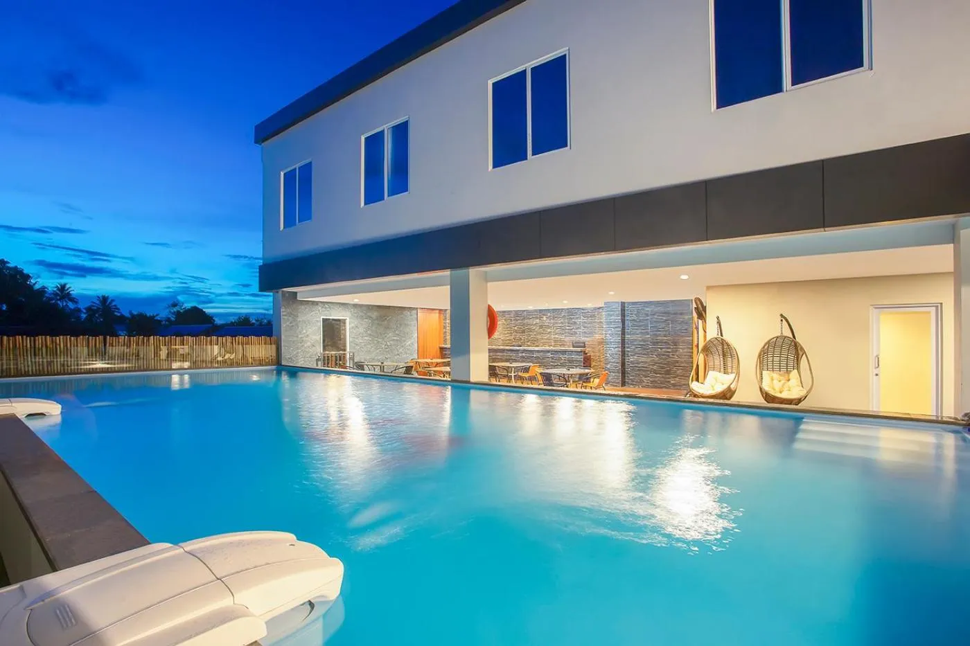 Piscine illuminée devant un bâtiment moderne au crépuscule.