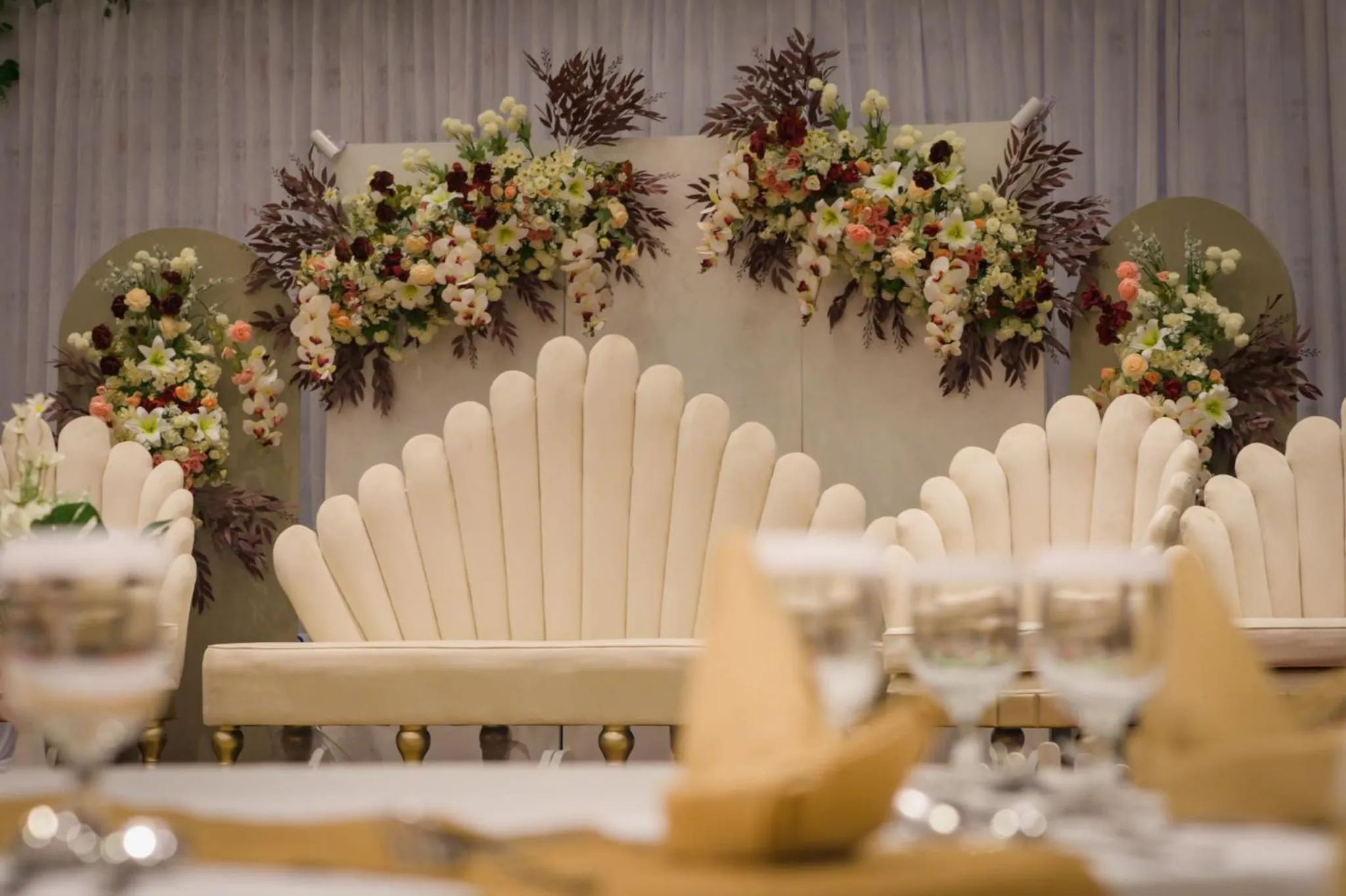 Une table dressée avec des verres et des serviettes devant un décor floral et un canapé blanc.