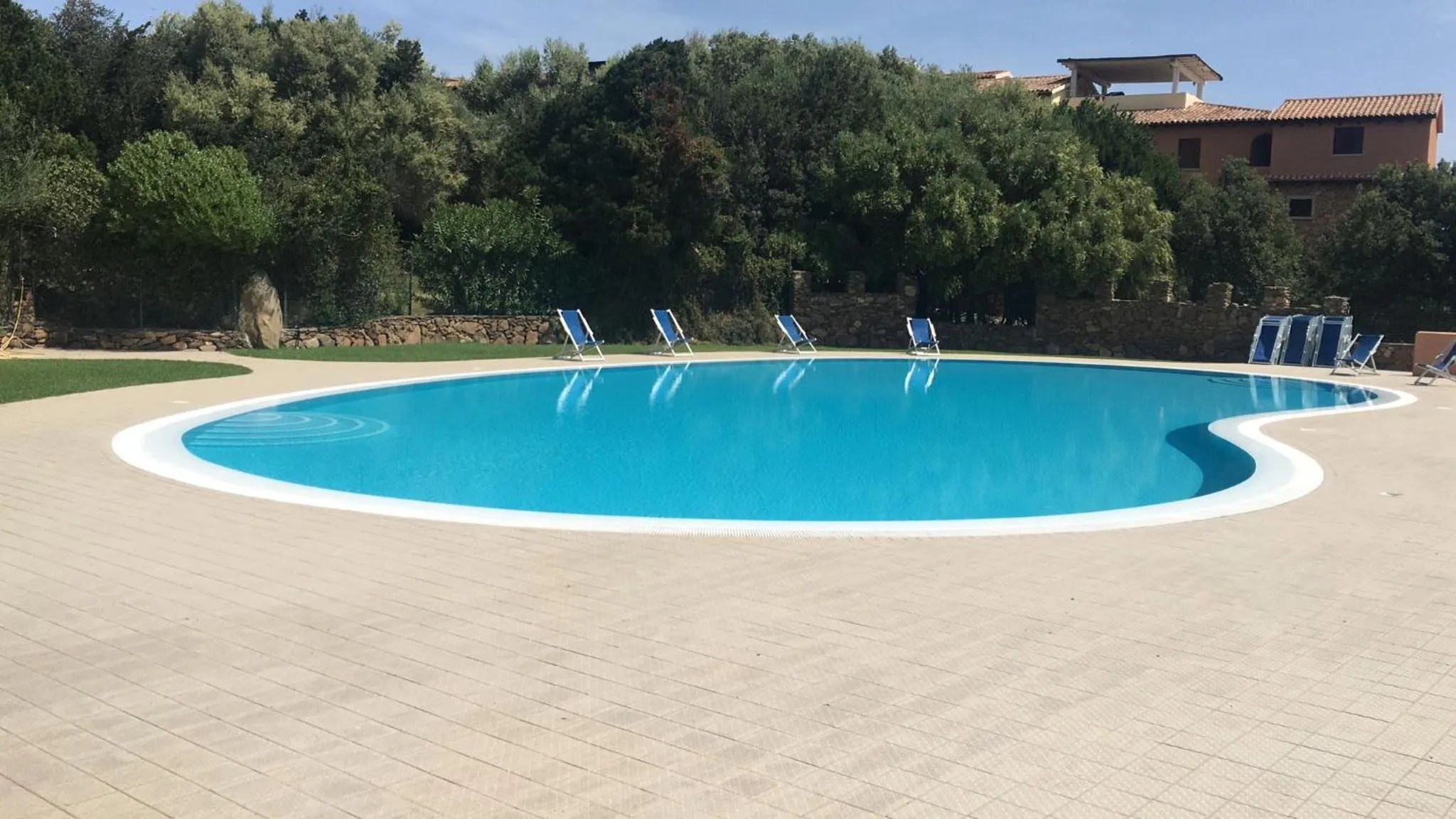Une piscine rectangulaire avec des transats bleus sur une terrasse ensoleillée.