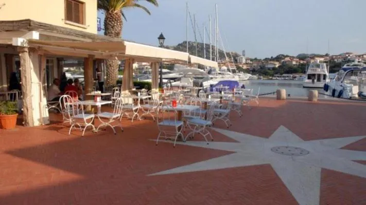 Terrasse ombragée avec tables et chaises en bord de port.