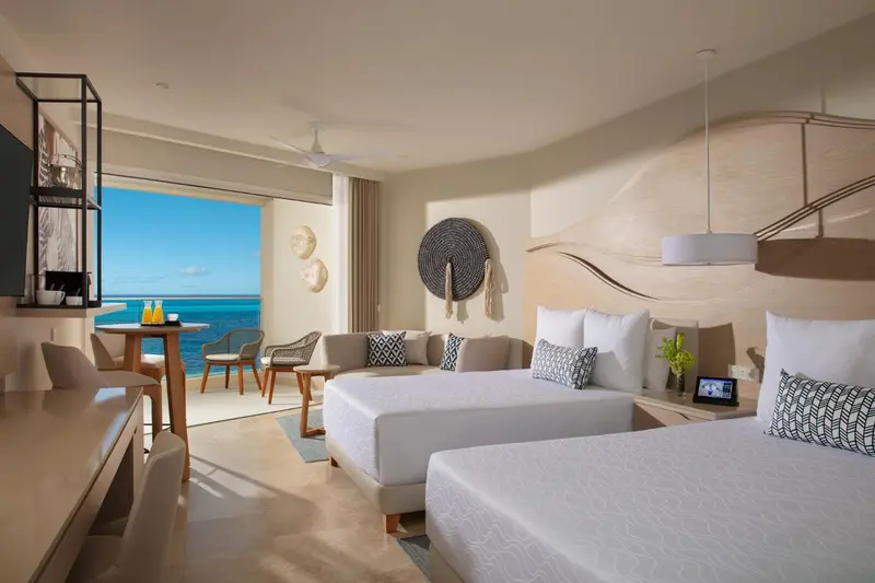 Une chambre lumineuse avec un lit double et un coin salon donnant sur la mer.