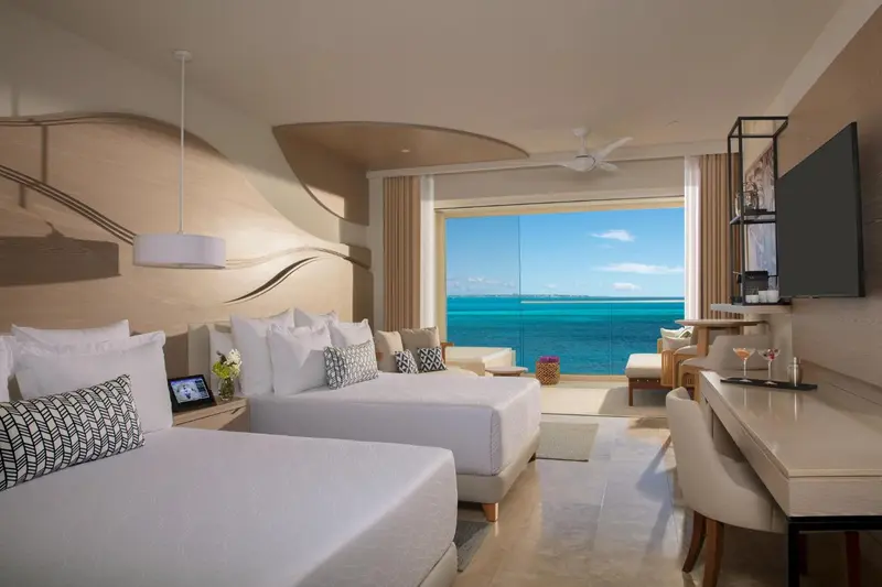 Chambre lumineuse avec deux lits et vue sur la mer.